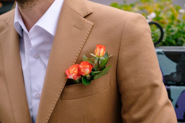 Close-up man dressed in classy jaket with three roses in poket