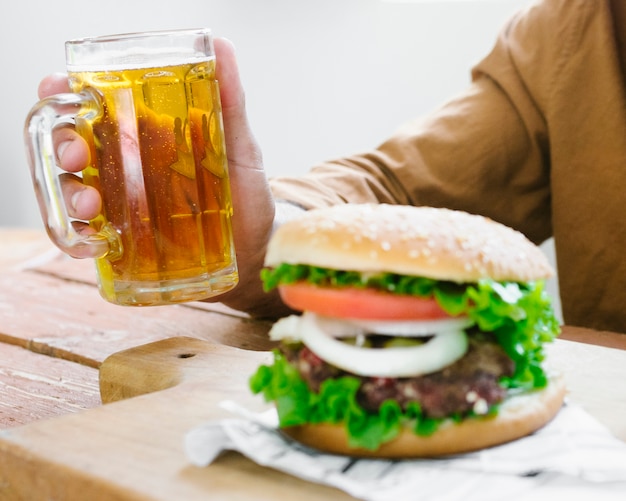 Uomo del primo piano che beve birra e che mangia hamburger