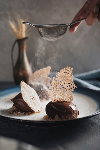 Close-up of a man dusting the sugar on delicious chocolate pastry