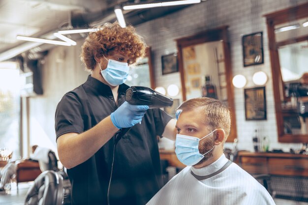 コロナウイルスのパンデミック中にマスクを身に着けている理髪店で髪を切る男を閉じます。