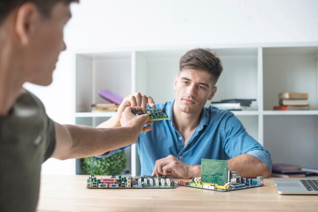 Close-up of man giving circuit board to his friend working with hardware equipment