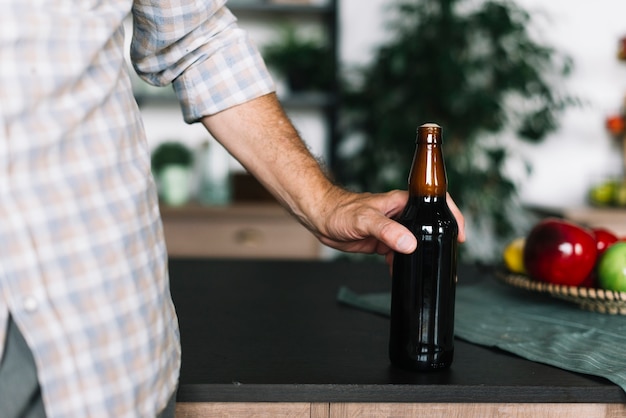 Close-up of a man holding beer bottle on kitchen counter