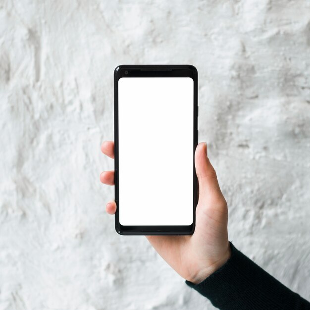 Close-up of a man holding a blank smart phone screen against white concrete wall