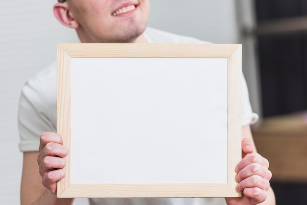 Close-up of a man holding blank white picture frame in front of camera