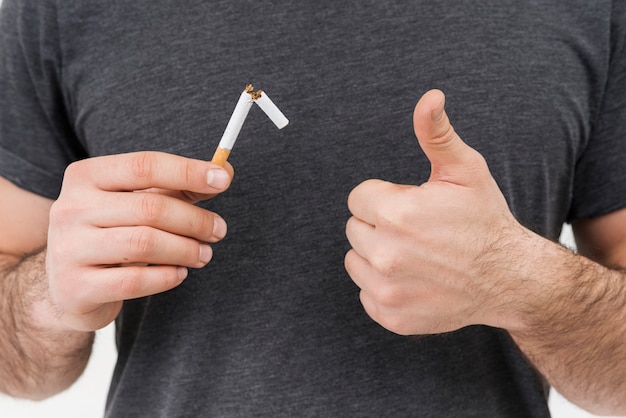 Крупным планом мужчина держит сломанную сигарету, показывая большой палец вверх знак