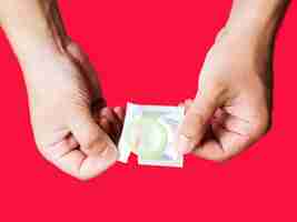 Бесплатное фото Крупным планом мужчина держит презерватив с красным фоном