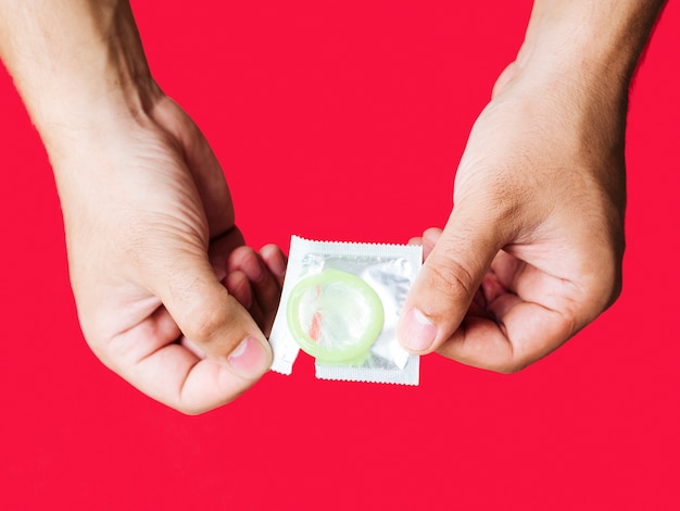 Close-up man holding condom with red background