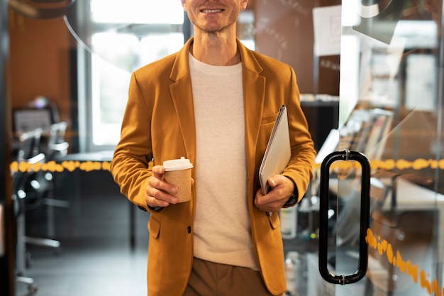 Крупным планом мужчина держит ноутбук и чашку кофе
