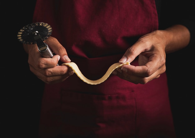 Close-up man holding pizza cutter and dough 