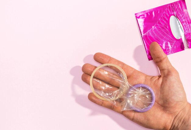 Крупным планом мужчина держит развернутые презервативы