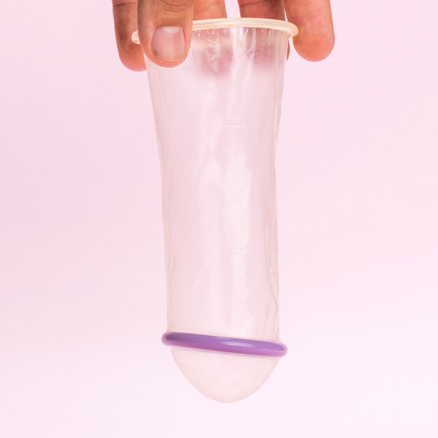 Close-up man holding an unwrapped transparent condom