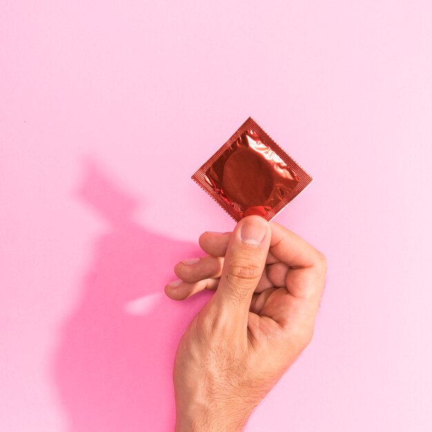 Close-up man holding up a red condom 