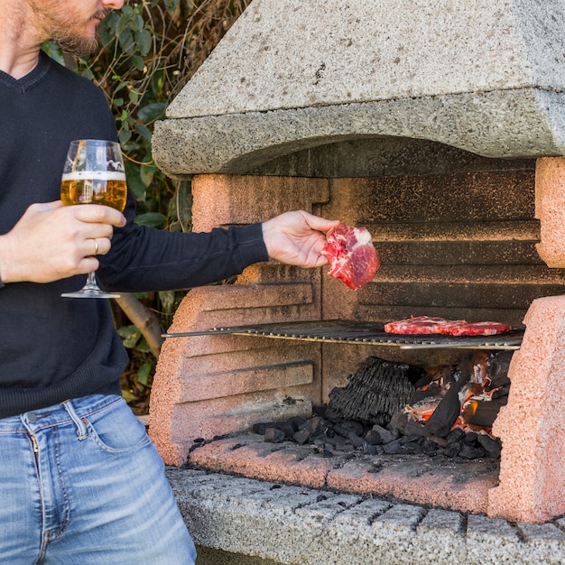 Close-up of man holding wineglass grilling beef in barbecue