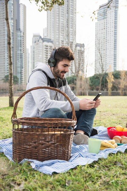 ピクニック、携帯電話を使用してヘッドフォンで音楽を聴く男のクローズアップ