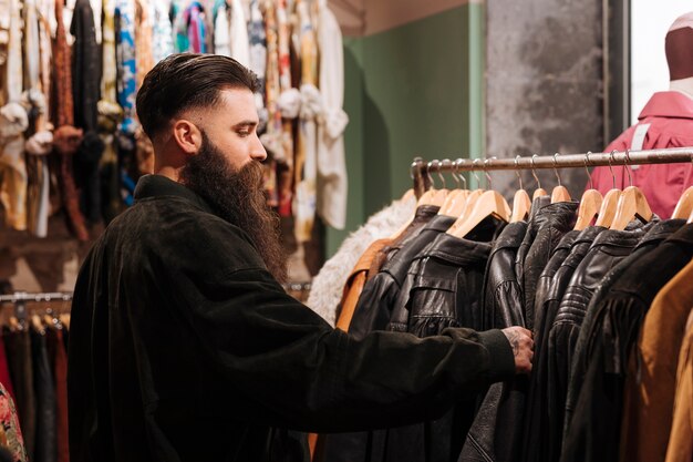 Close-up of a man looking at the leather jacket on the rail in the clothing shop