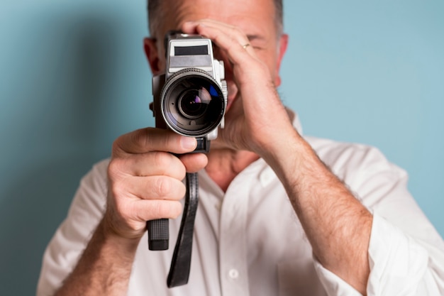 Close-up of a man looking through 8mm film camera against blue backdrop