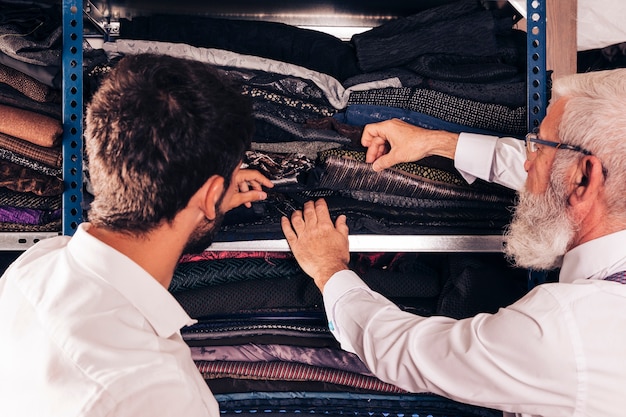 Free photo close-up of man and male senior tailor selecting the fabric in the shelf