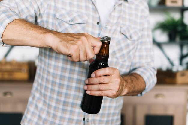 オープナでビール瓶を開けている男性のクローズアップ