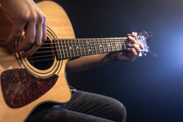 Close-up of a man playing an acoustic guitar in the dark with stage lighting.