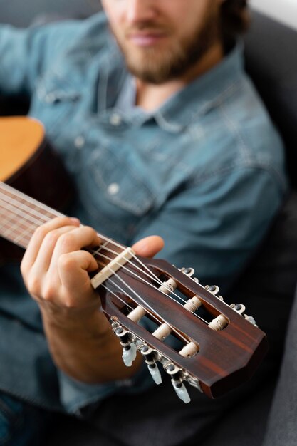 Крупным планом человек играет на гитаре дома