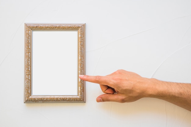 Close-up of man pointing at white golden picture frame on wall