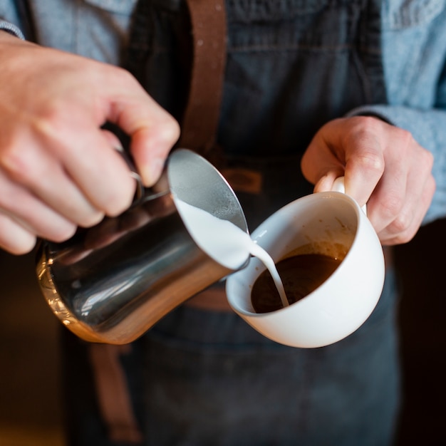 一杯のコーヒーに牛乳を注ぐ男のクローズアップ