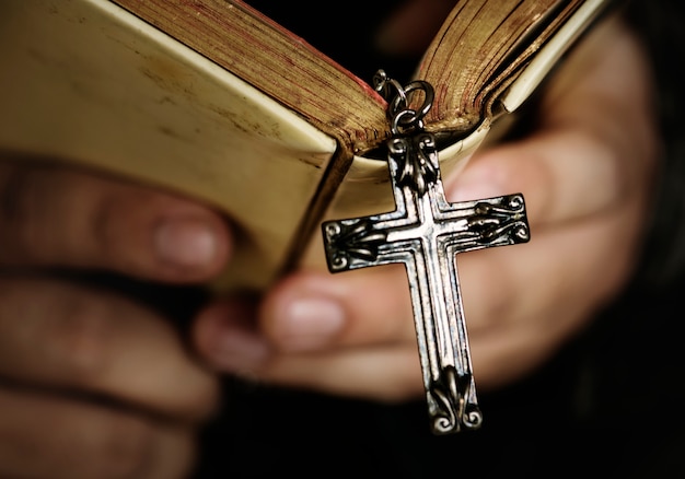 Close up of a man reading a bible with cross hanging religion and belief concept