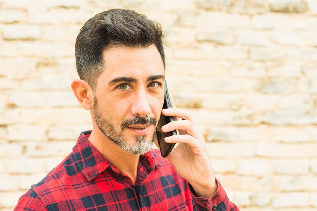 Close-up of man in red plaid shirt talking on mobile phone looking at camera