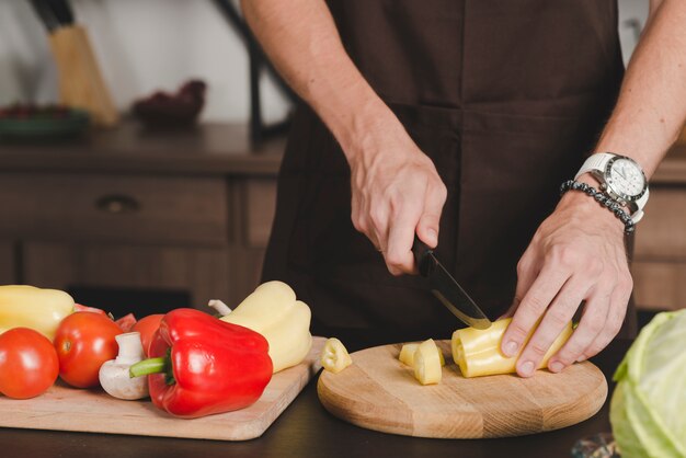 Close-up of man's hand cutting bellpepper with knife on chopping board