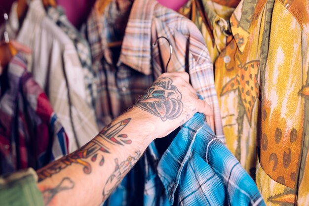 Close-up of man's hand holding the blue shirt on the rail in the clothing shop