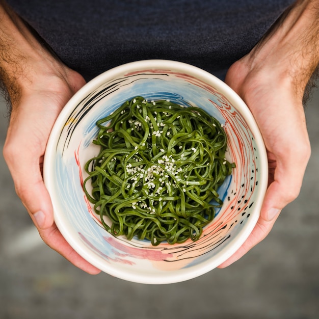 Close-up of a man's hand holding bowl of seaweeds with sesame seeds