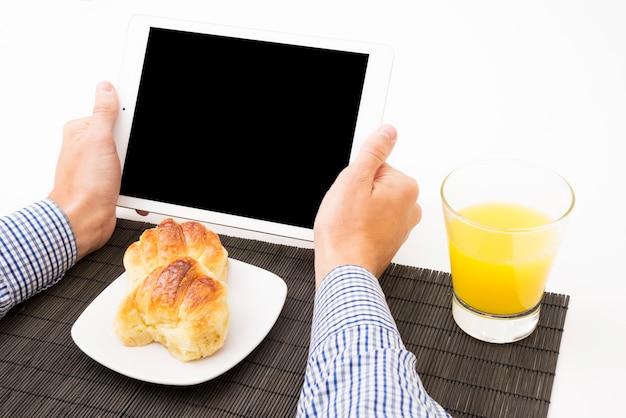 Close-up of man's hand holding digital tablet with blank screen at breakfast time