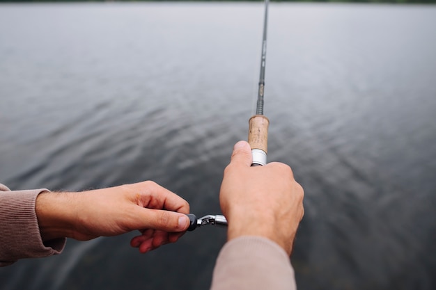 Primo piano della canna da pesca della tenuta della mano dell'uomo sopra il lago