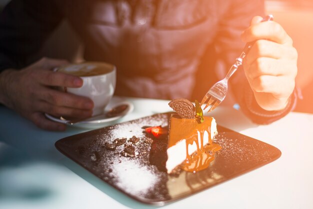 Close-up of man's hand holding fork in the cake slice