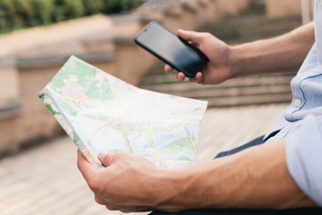 Крупный план мужской руки, держащей карту и сотовый телефон на открытом воздухе