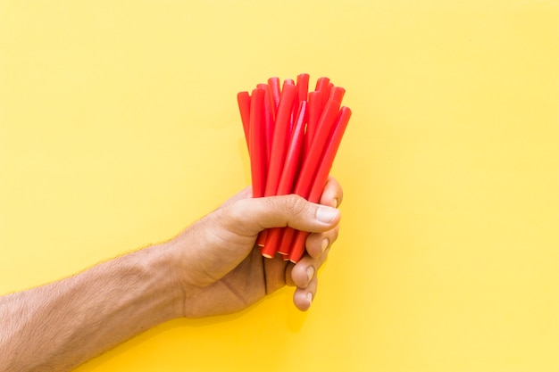 Close-up of man's hand holding red licorice candies against yellow background
