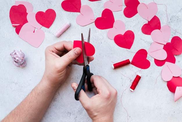 Close-up of man's hand making the heart shape garland on white textured backdrop