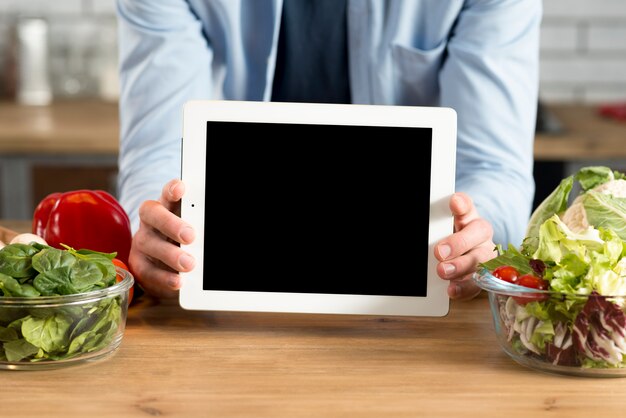 キッチンで空白の画面を持つデジタルタブレットを示す人間の手のクローズアップ