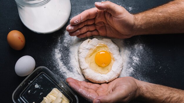 Close-up of man's hand with egg york over the dough