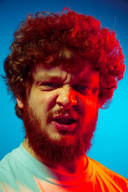 Close up man's portrait isolated on blue studio wall in red neon light