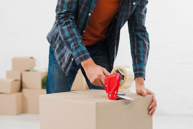 Close-up of a man sealing cardboard box with duct tape