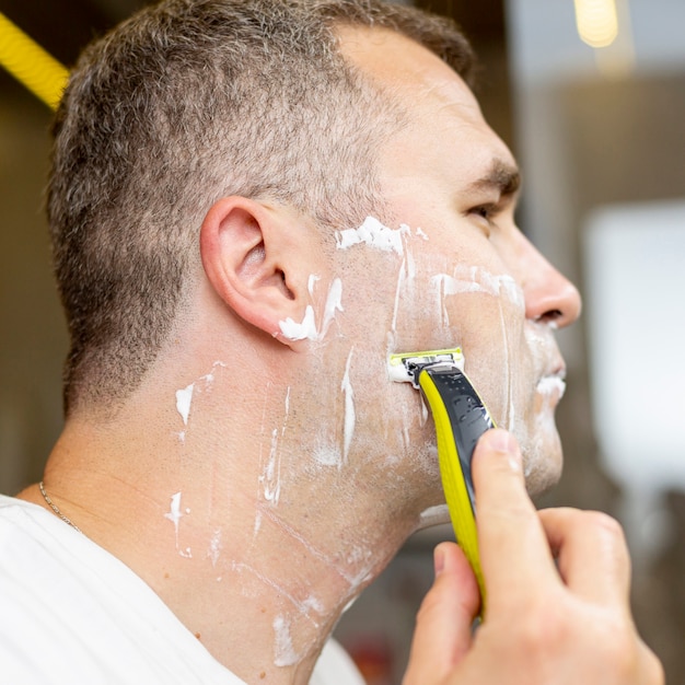 Close-up man shaving indoors