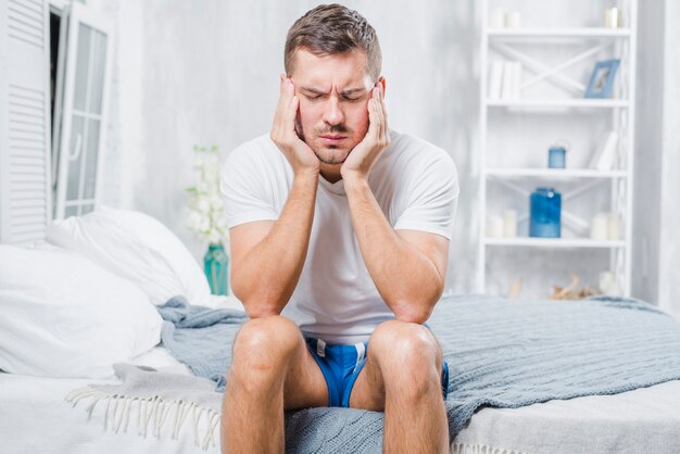 Close-up of a man sitting on bed having headache