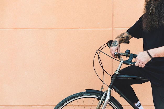 Primo piano di un uomo seduto sulla bicicletta contro il muro beige