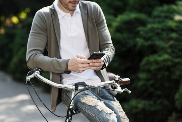 携帯電話を使って自転車のハンドルに座っている男のクローズアップ