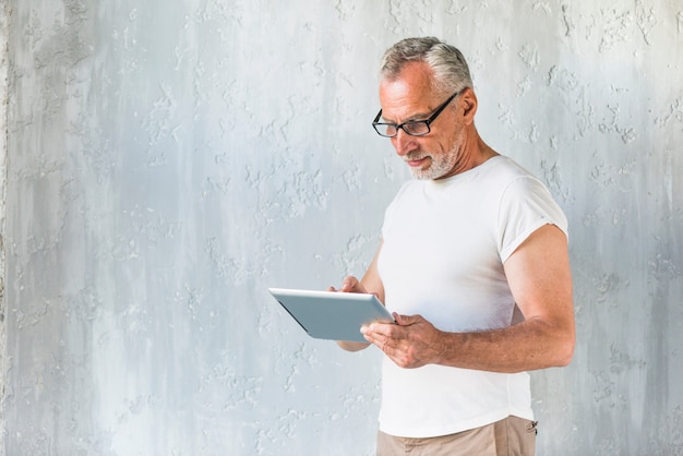 Close-up of man standing in front of concrete wall using digital tablet