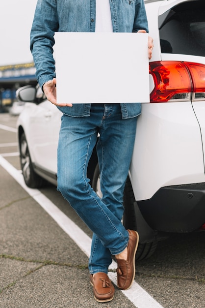 Close-up of a man standing near the car on road showing blank white placard