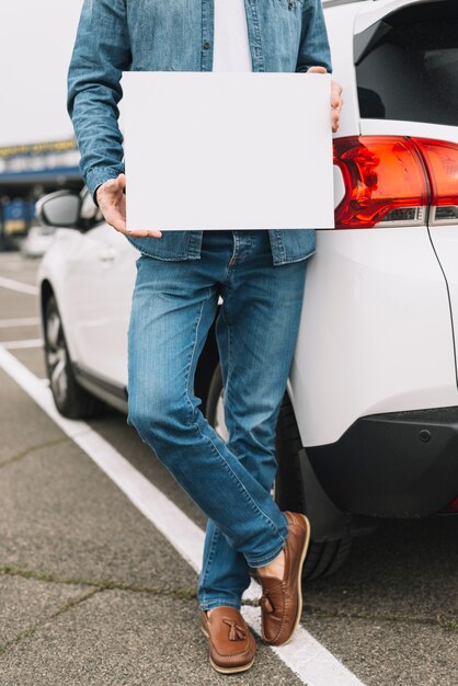 Крупный план человек, стоящий рядом с автомобилем на дороге, показывающий пустой белый плакат