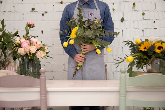 Foto gratuita primo piano di un uomo in piedi dietro il tavolo tenendo il bouquet di fiori in mano