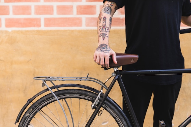 Foto gratuita primo piano di un uomo in piedi con la bicicletta di fronte al muro